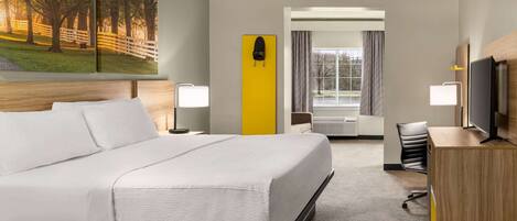 A hotel room with a large bed, a desk with a computer, a TV, and a painting on the wall.