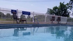 Una piscina con agua cristalina, rodeada por una valla blanca y sillas de descanso.