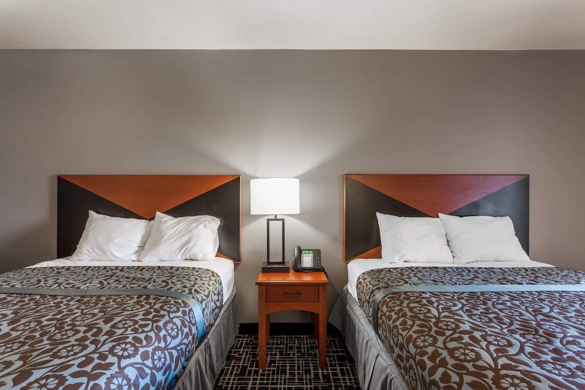 Ein Hotelzimmer mit zwei Betten, einem Nachttisch mit Lampe und Telefon sowie einem gemusterten Boden.