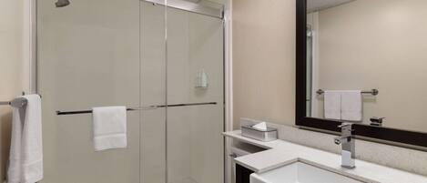 A modern bathroom with a glass shower enclosure, a white sink, and a large mirror.