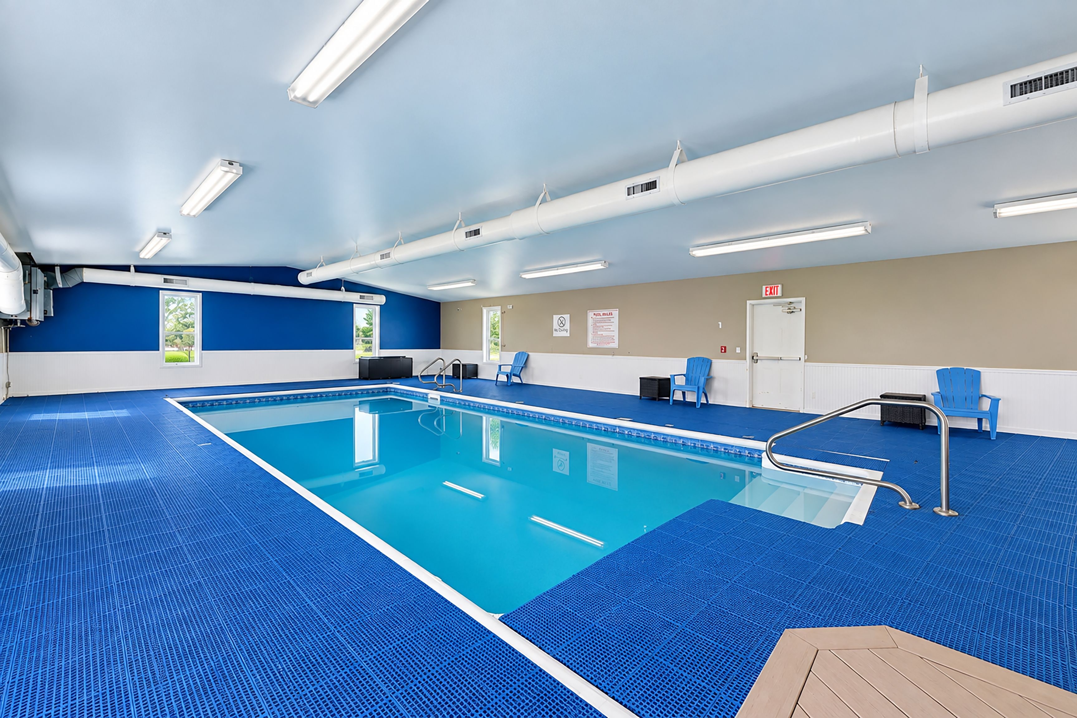 Una piscina con suelo de baldosas azules, rodeada de paredes en una combinación de colores azul y beige, y un techo con iluminación fluorescente.