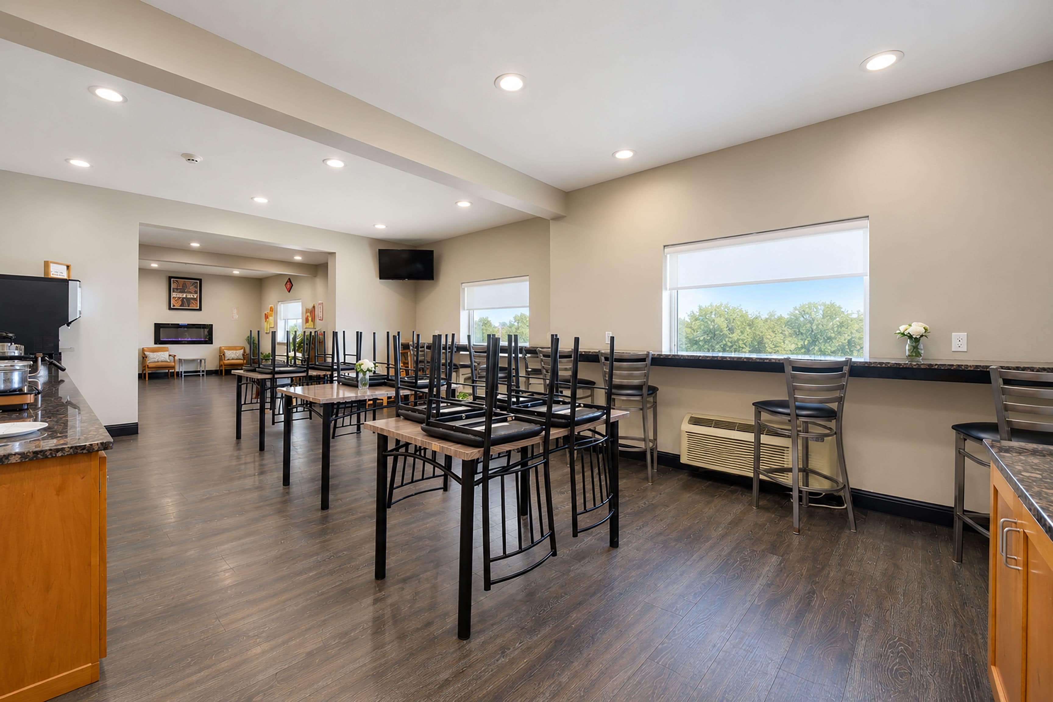 A modern kitchen with a dining area, wooden flooring, and a large window offering a view.