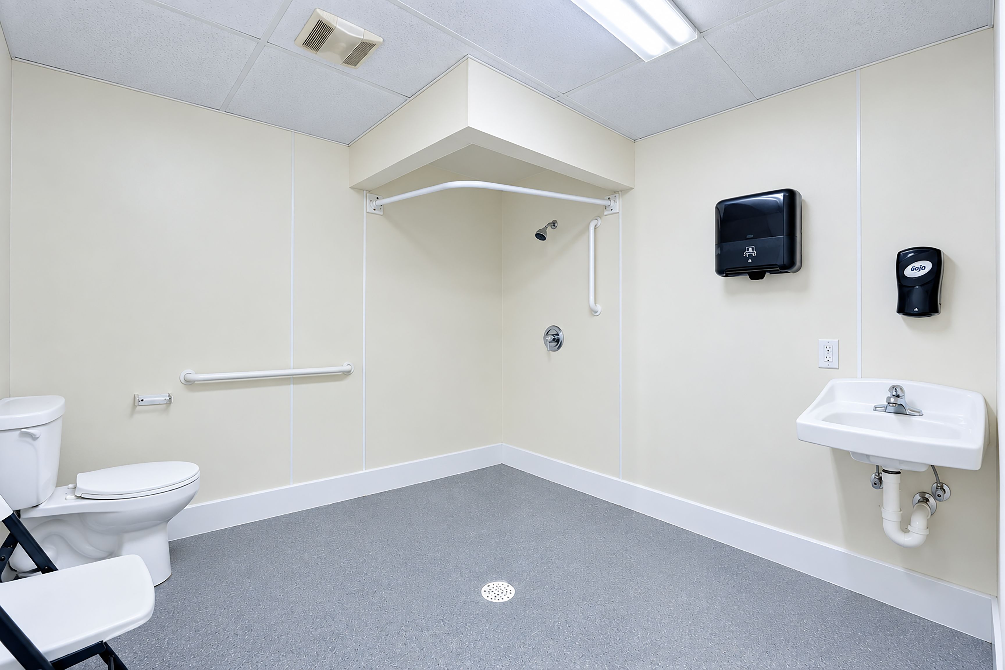 A bathroom with a toilet, a sink, a shower, and a hand sanitizer dispenser.