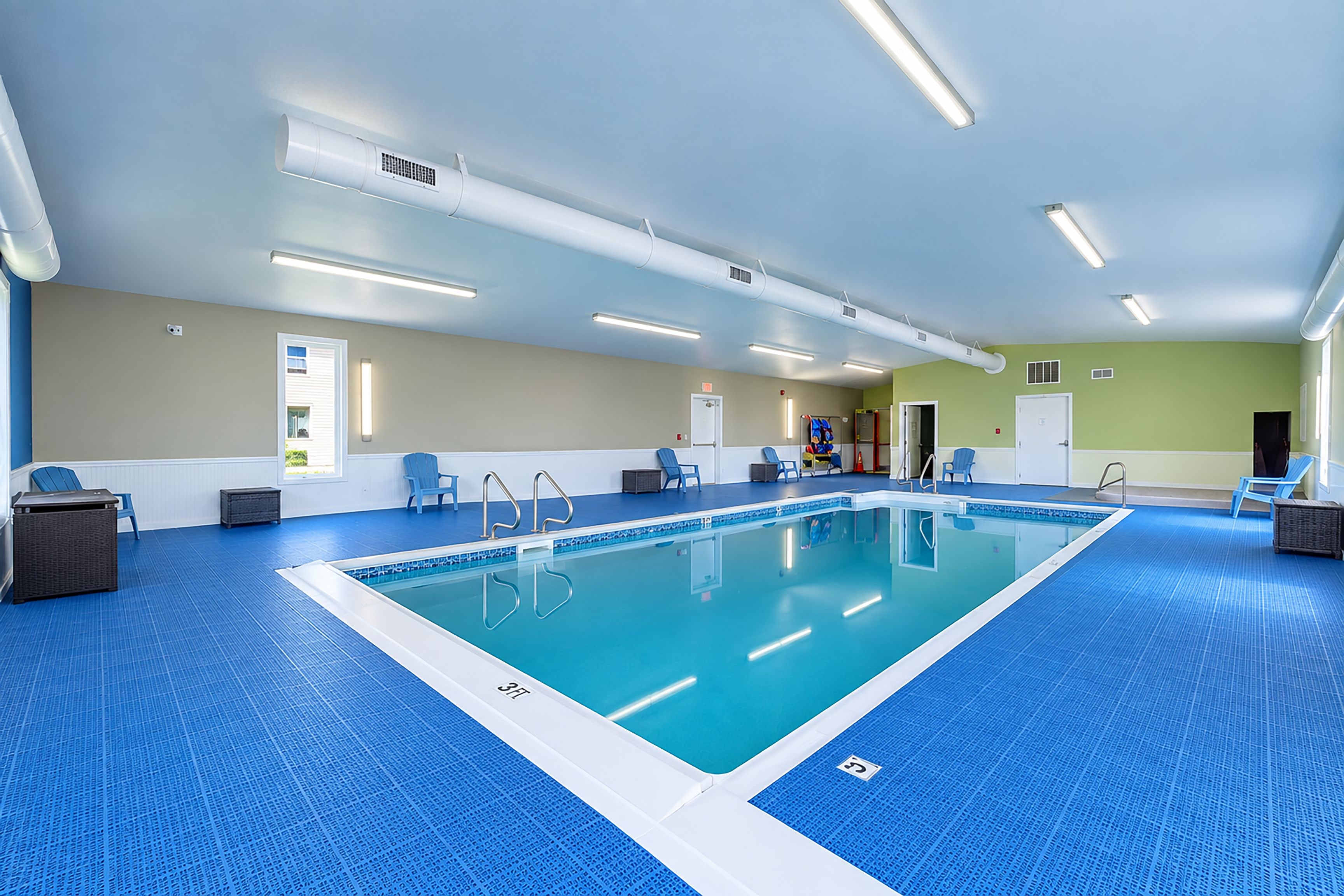 An indoor swimming pool with clear lanes, blue flooring, and overhead lighting.