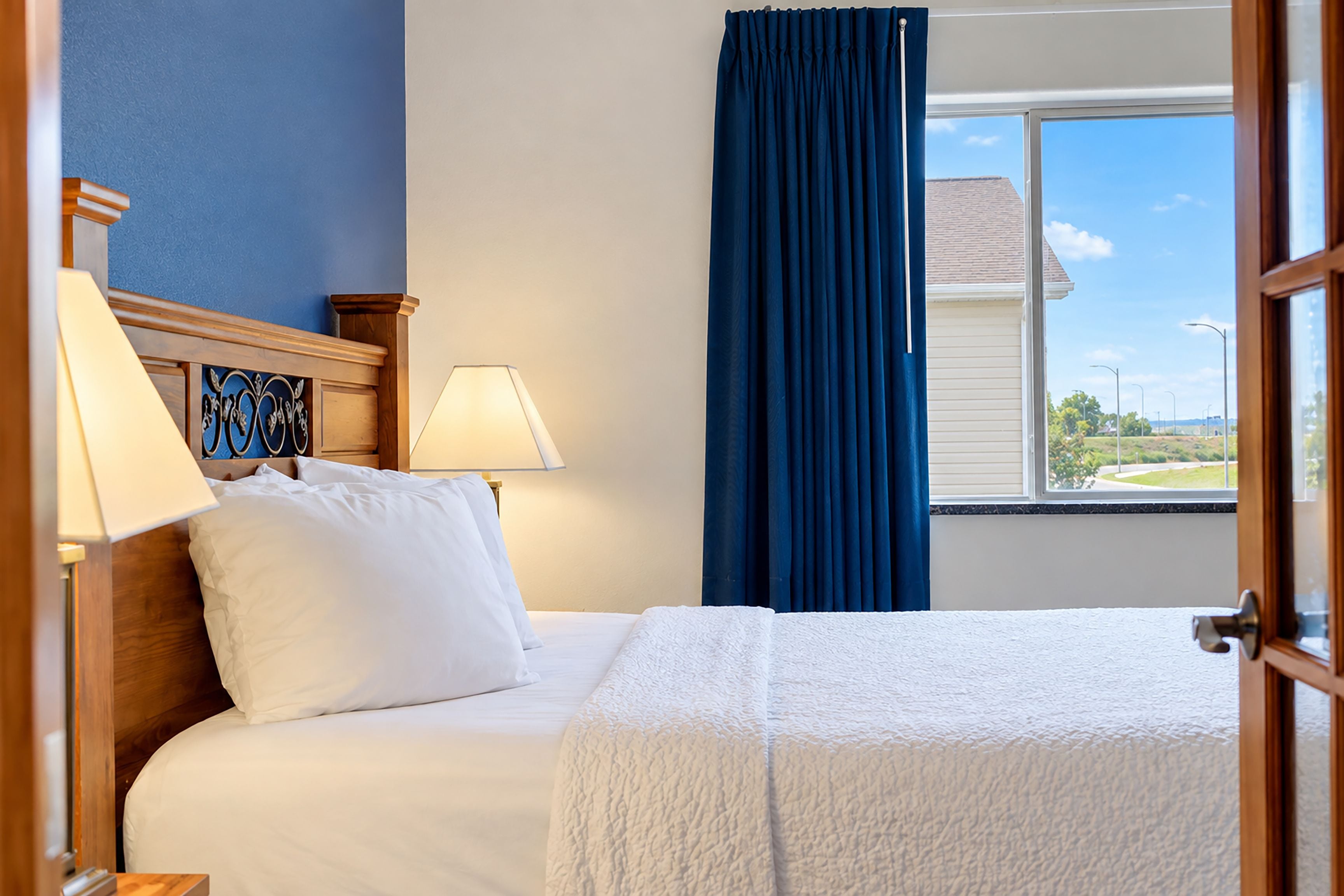 A hotel room with a bed, two bedside lamps, a window with a view of the outside, and a curtain.