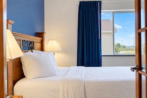 A hotel room with a bed, two bedside lamps, a window with a view of the outside, and a curtain.