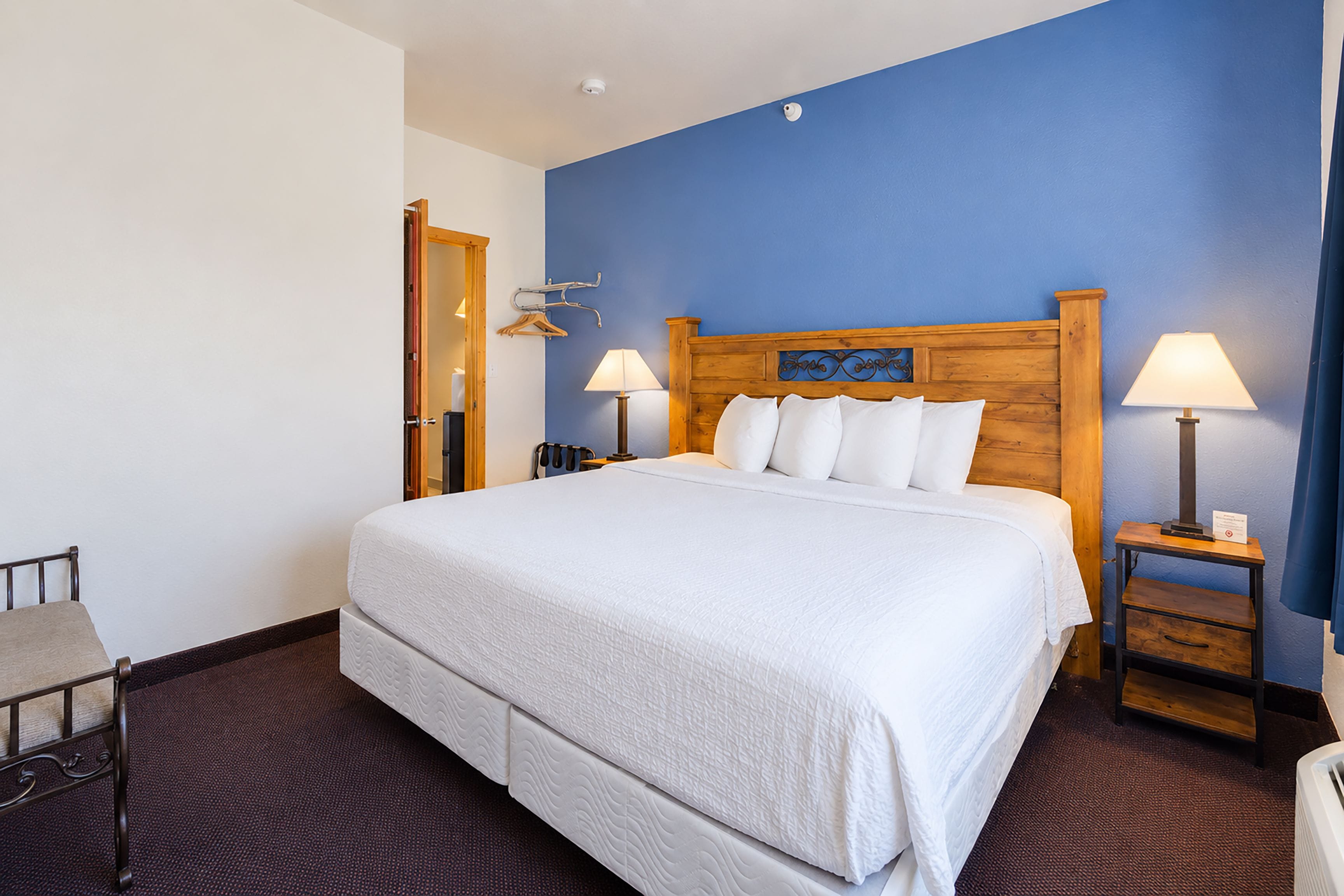 Een hotelkamer met een groot bed, twee nachtkastjes met lampen, een houten hoofdbord en een blauwe accentmuur.