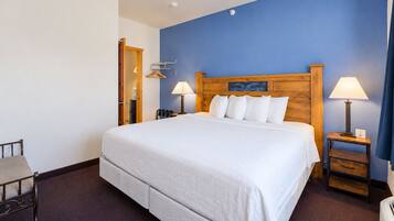 A hotel room with a large bed, two bedside tables with lamps, a wooden headboard, and a blue accent wall.
