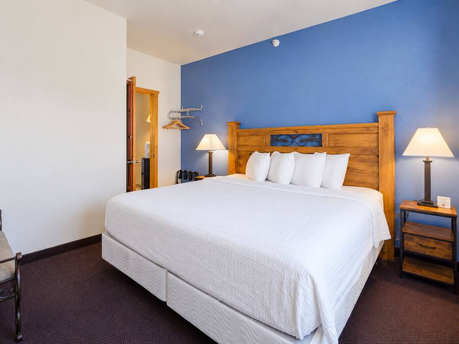 A hotel room with a large bed, two bedside tables with lamps, a wooden headboard, and a blue accent wall.