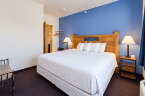 A hotel room with a large bed, two bedside tables with lamps, a wooden headboard, and a blue accent wall.