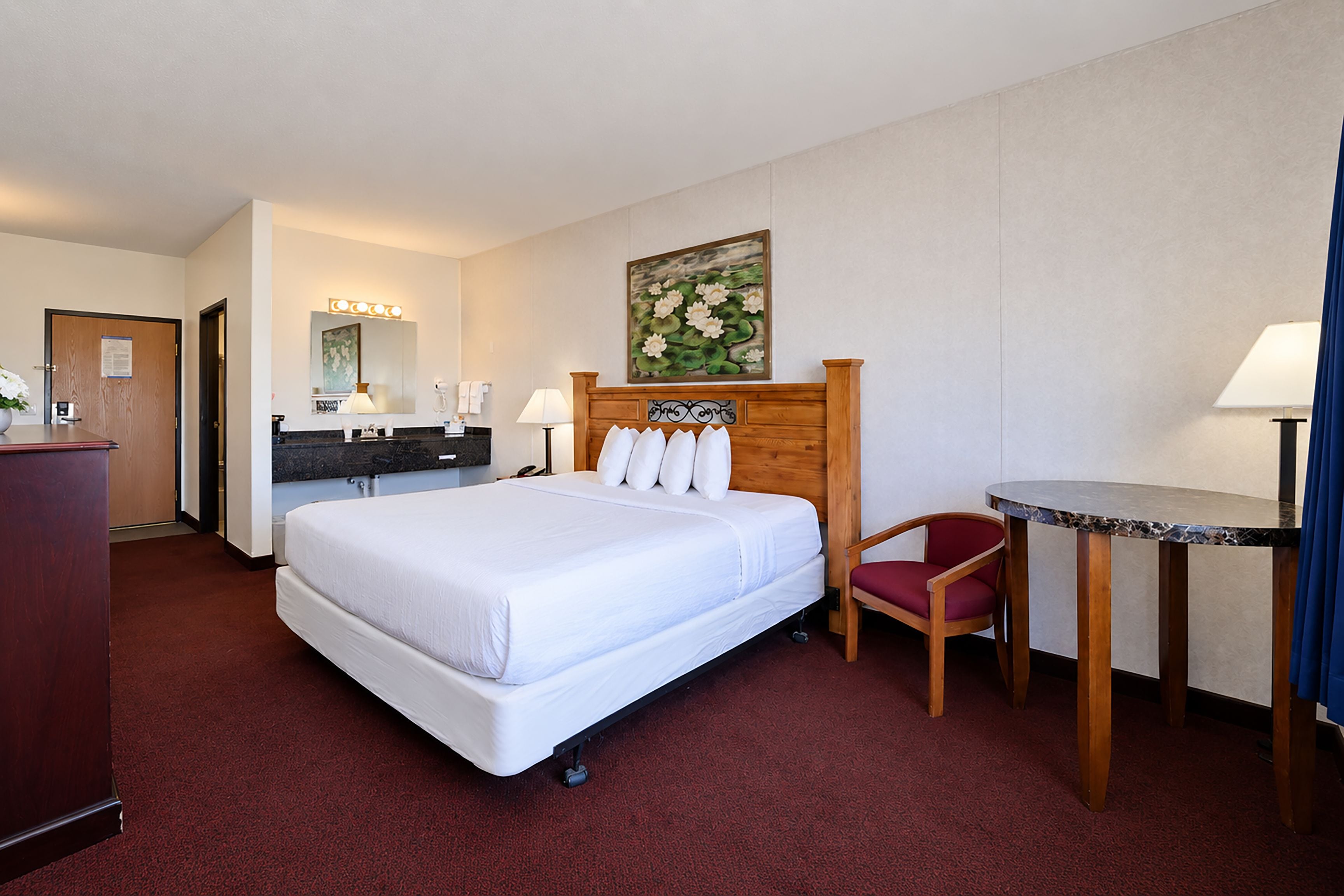 Habitación de hotel con una cama grande, un escritorio, una silla, un aparador, un espejo y un cuadro en la pared.