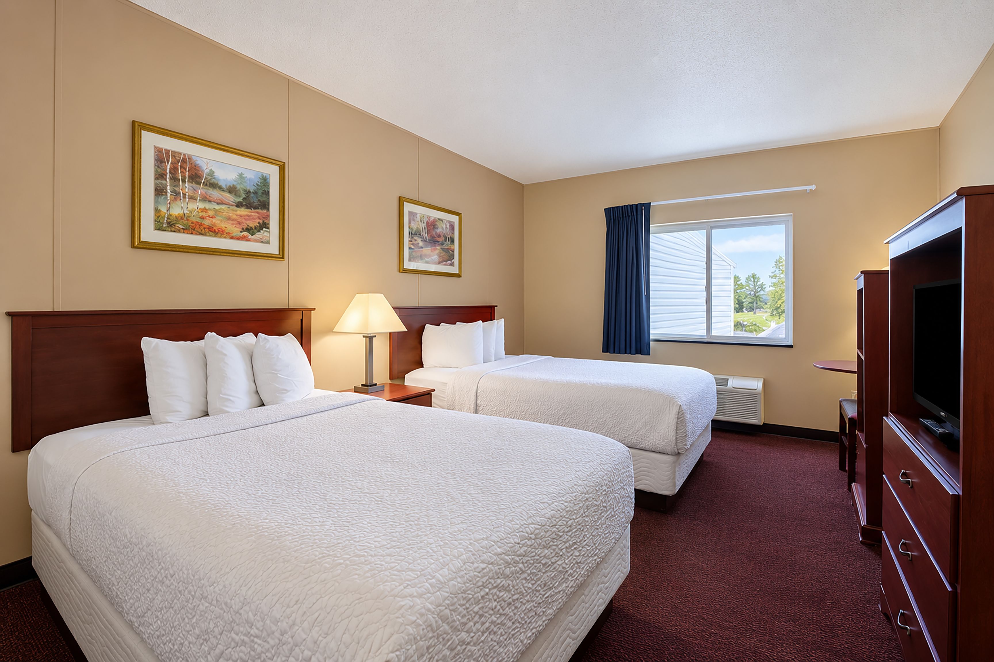 A hotel room with two beds, a television, and a window with curtains.