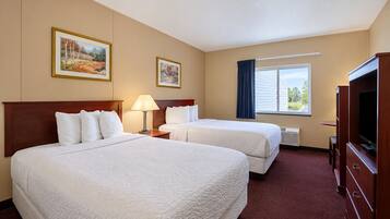 A hotel room with two beds, a television, and a window with curtains.