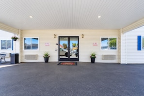 A building entrance with a no smoking sign, potted plants, and a black mat at the door.