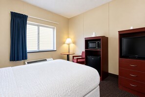 Habitación de hotel con cama, televisor, escritorio con lámpara y minibar.