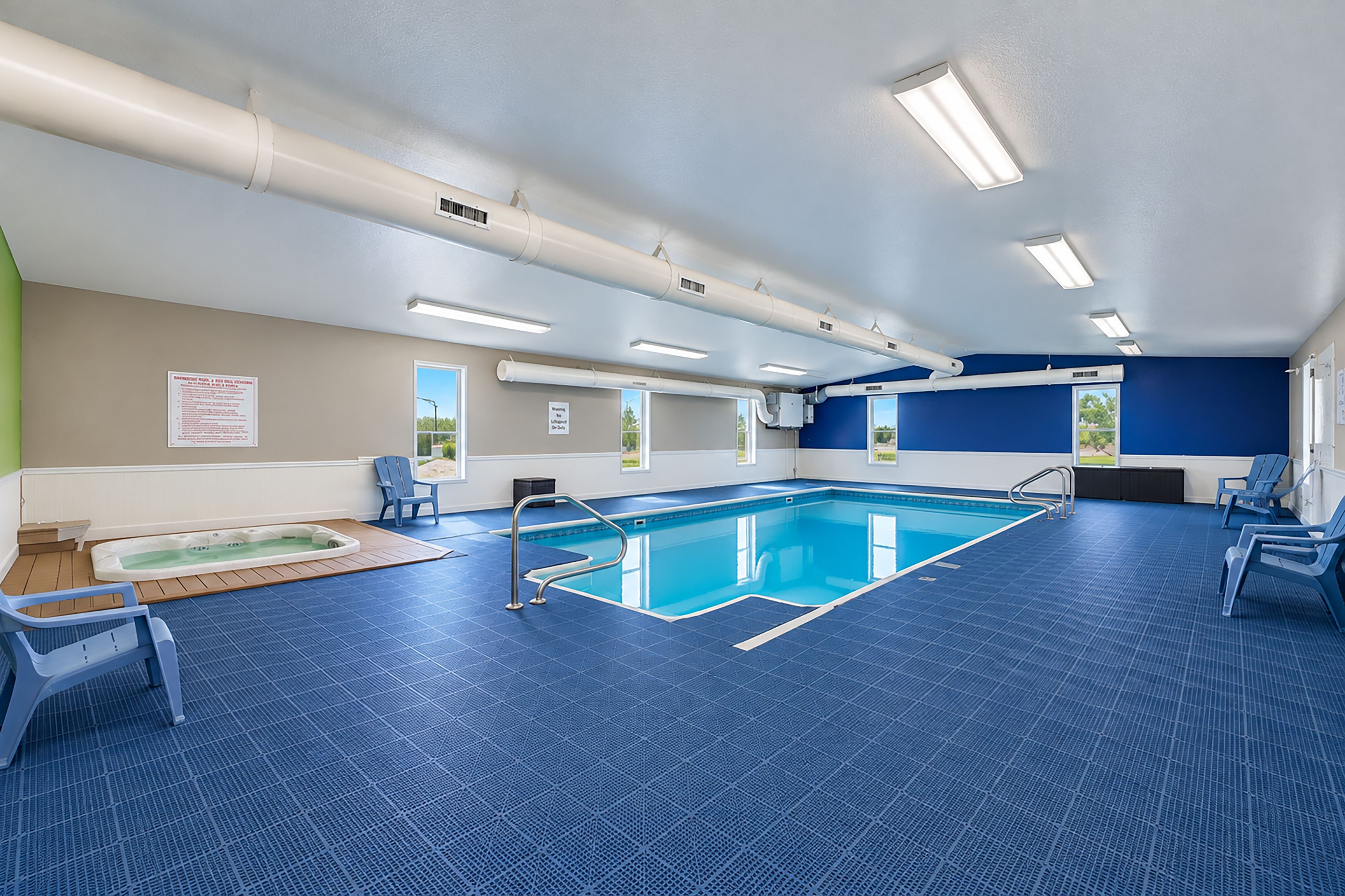 Een zwembad met een jacuzzi, blauwe stoelen en uitzicht op de omgeving.