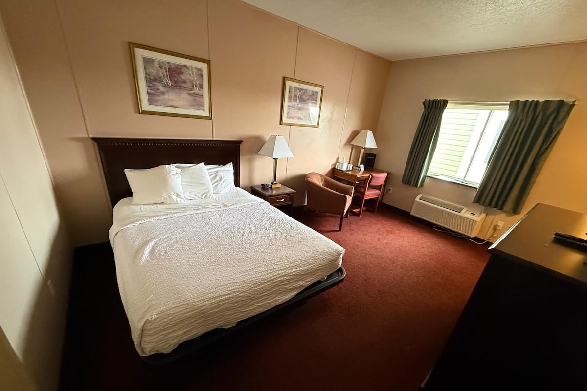 A hotel room with a bed, desk, chair, two framed pictures, and a window with curtains.