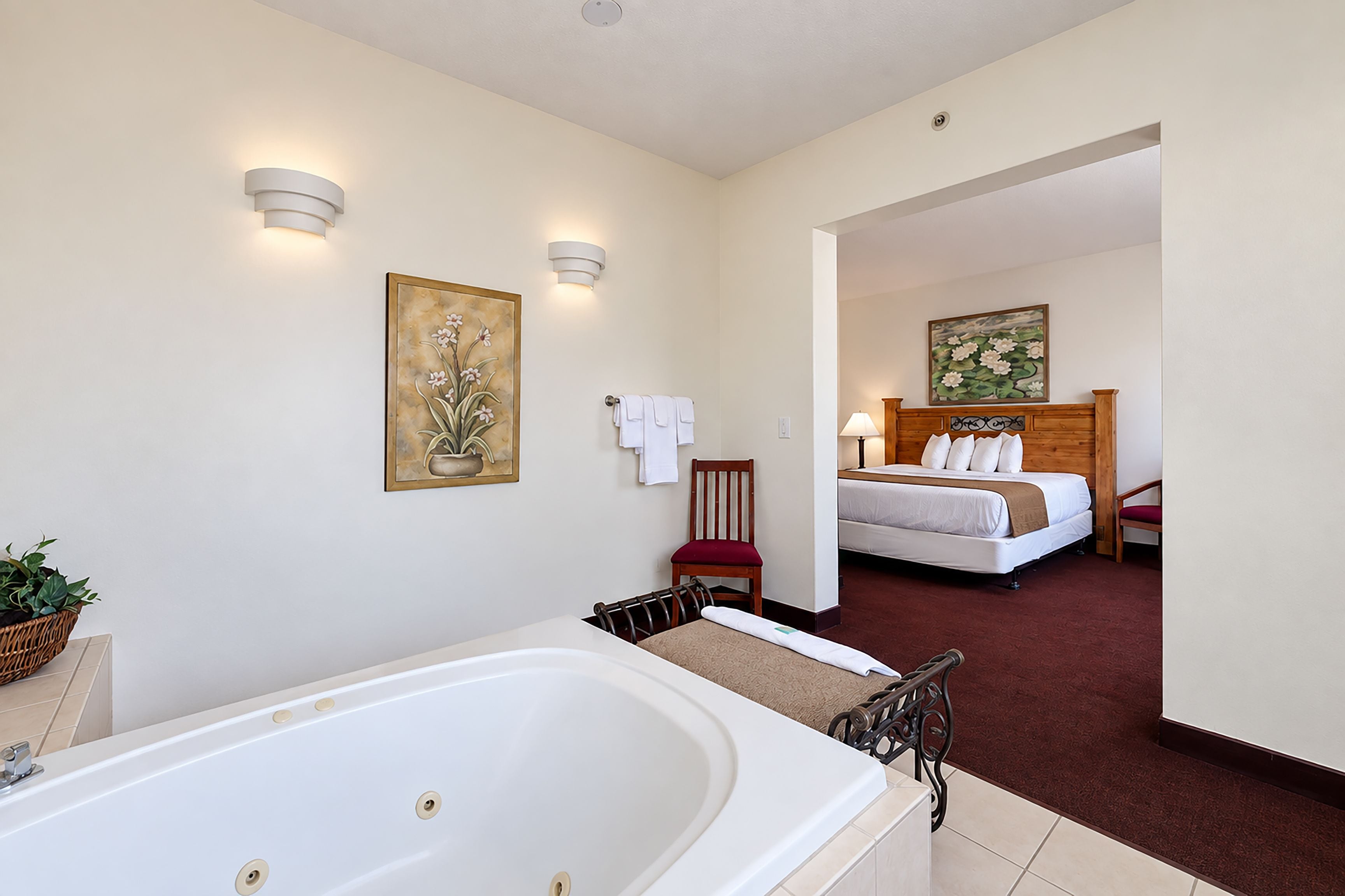 Habitación de hotel con una bañera grande, una cama con ropa blanca, un cabecero de madera y dos lámparas fijadas a la pared.