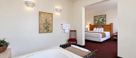 A hotel room with a large bathtub, a bed with white bedding, a wooden headboard, and two wall-mounted light fixtures.