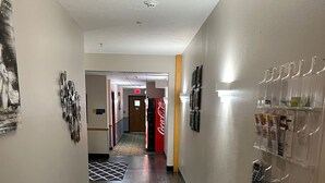 A hallway with a wooden floor, a Coca-Cola refrigerator, and a bulletin board with various items pinned to it.