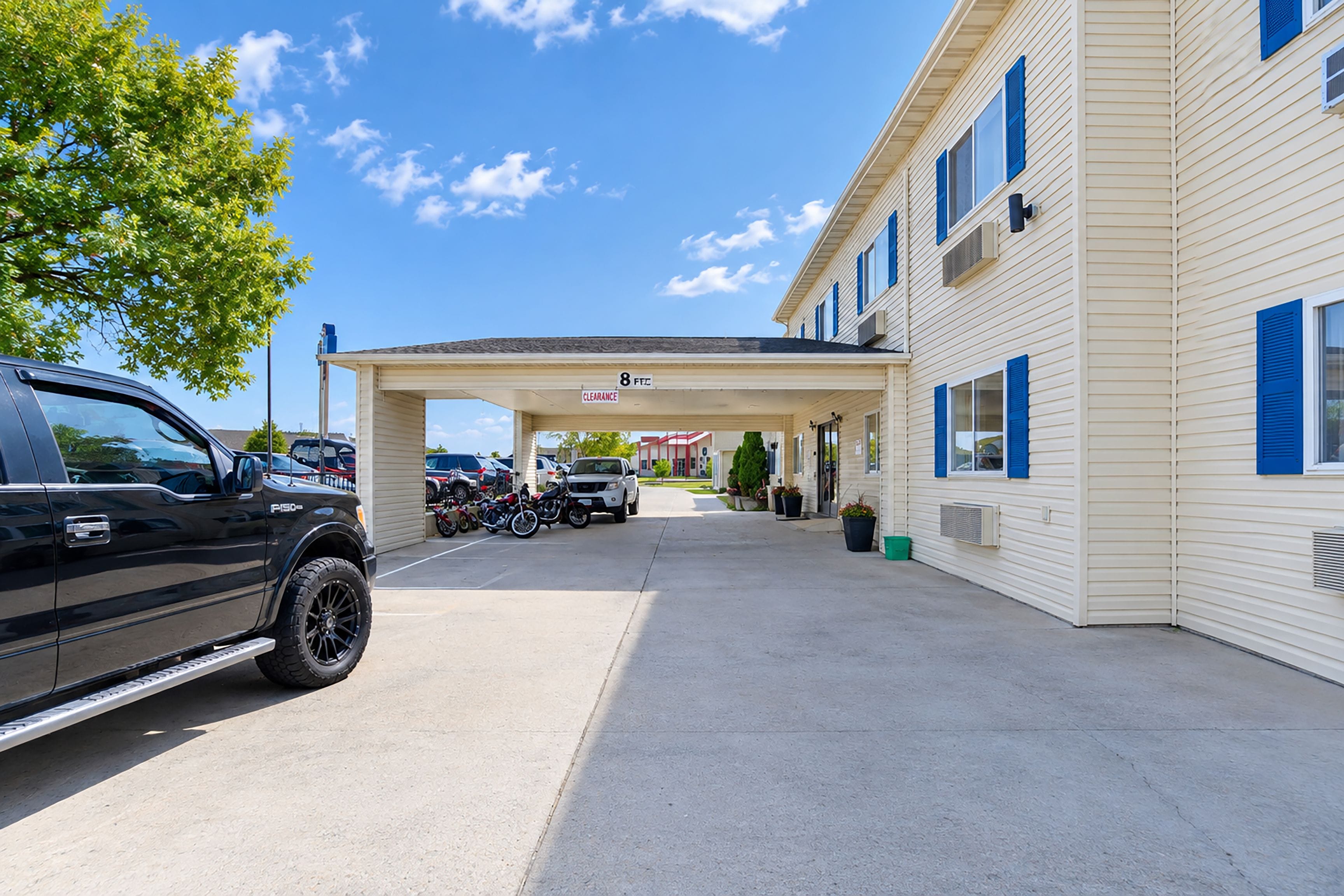 A motel with a covered parking area, a black pickup truck, and a row of parked motorcycles.