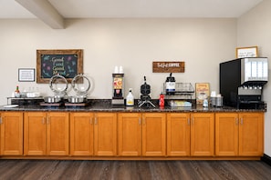 A kitchen area with a coffee station, a chalkboard with motivational writing, and a sign emphasizing coffee.