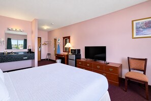 A hotel room with a bed, a desk with a TV, a chair, a dresser, a mirror, and a painting on the wall. - Fairbridge Inn & Suites Williston Near Airport (Williston)