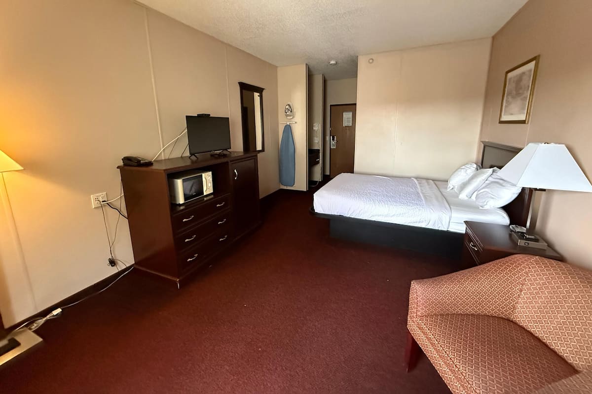 A hotel room with a bed, a dresser, a television, and a lamp.