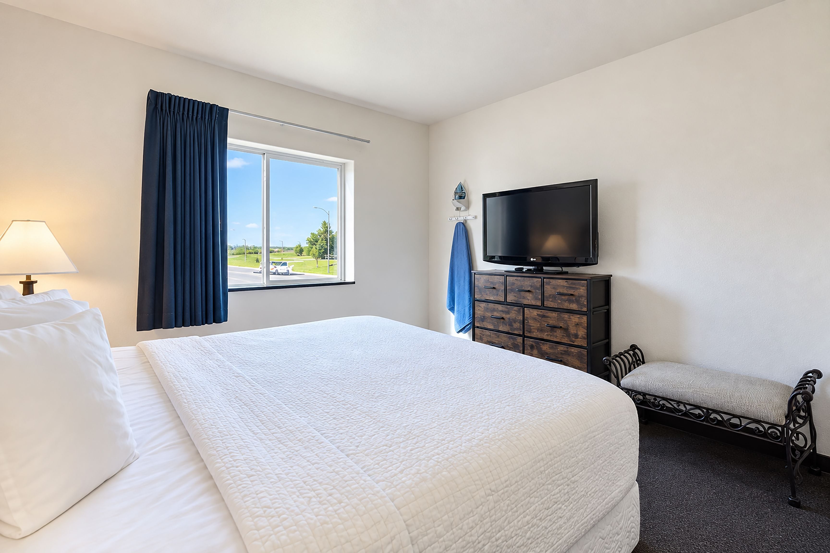 A hotel room with a bed, a television, a dresser, and a window with curtains.