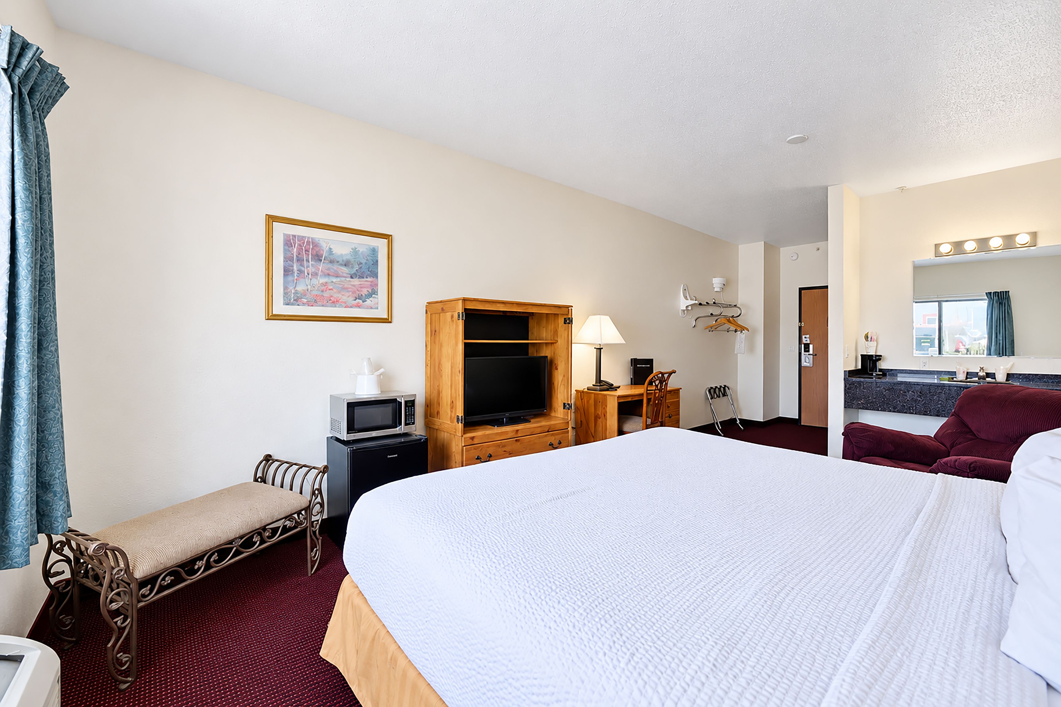 Ein Hotelzimmer mit einem großen Bett, einem Schreibtisch mit Computer, einem Fernseher und einem Gemälde an der Wand.