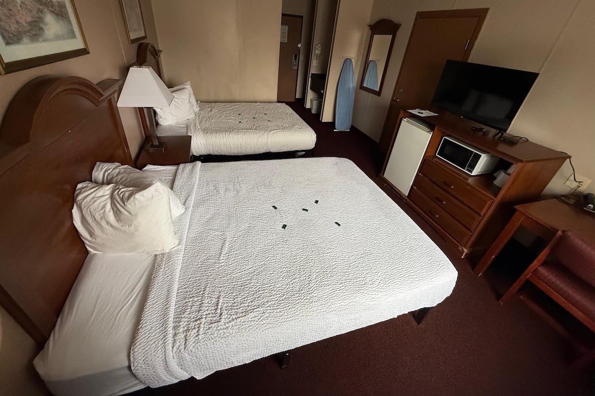 A hotel room with two beds, a television, a microwave, and a dresser.