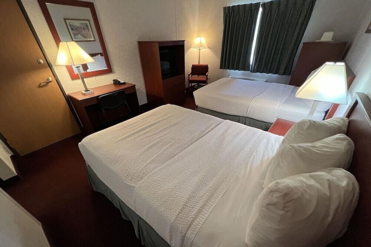A hotel room with two beds, a desk, a chair, and two lamps.