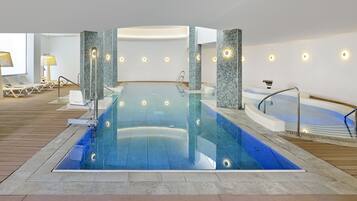 Une piscine intérieure moderne, dotée d’une eau cristalline, entourée de chaises longues et d’un jacuzzi.