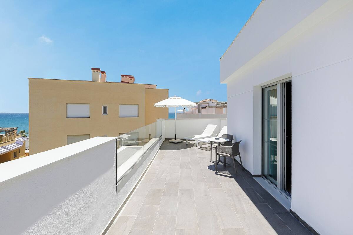 A balcony with a glass railing, a white umbrella, and a table with chairs.