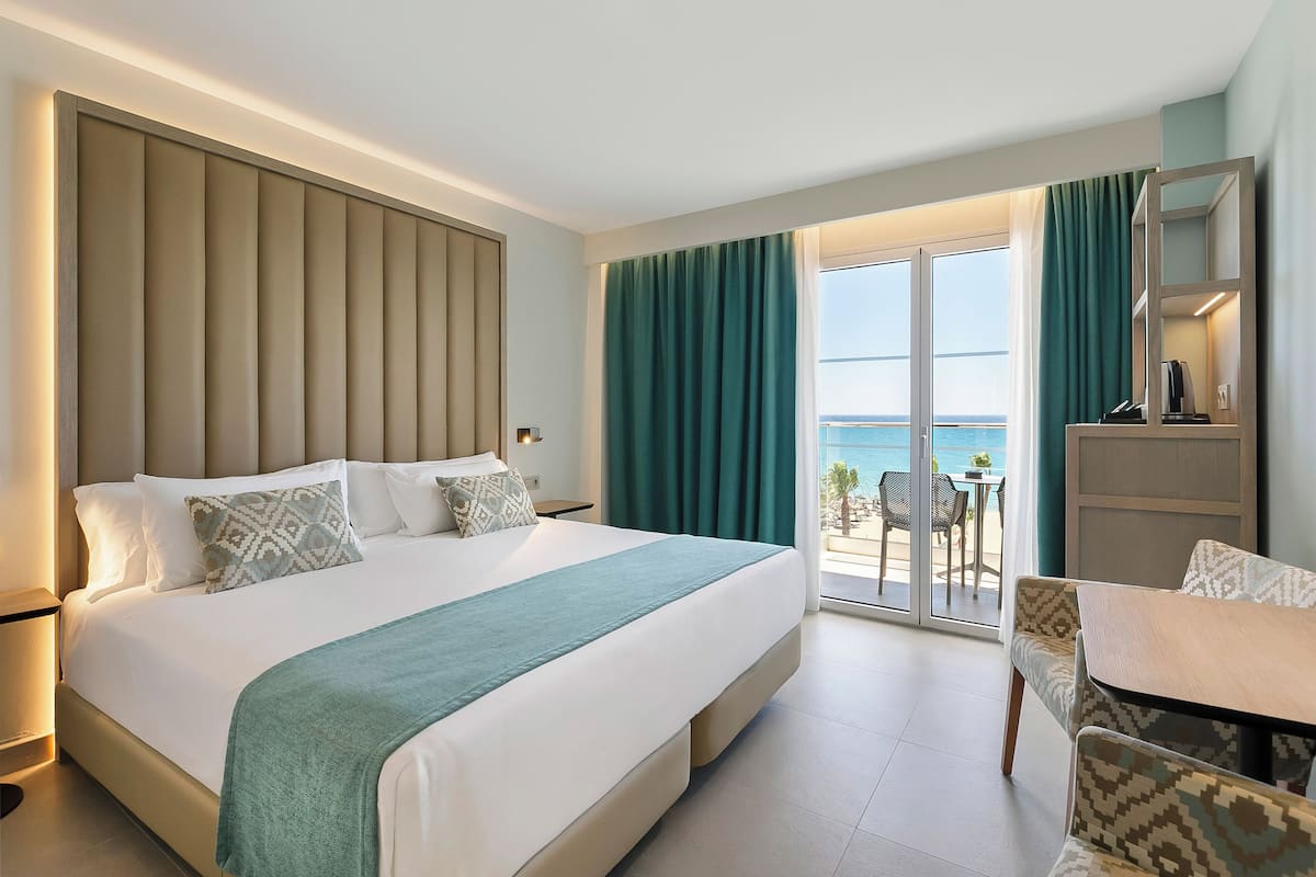 A hotel room with a large bed, a desk, and a view of the sea.