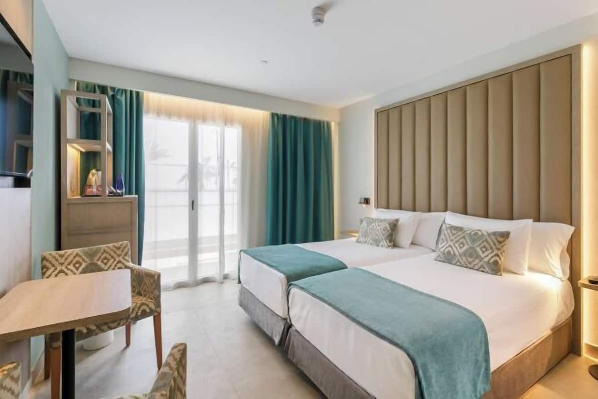 A hotel room with a bed, a desk, a chair, a wardrobe, and a window with curtains.