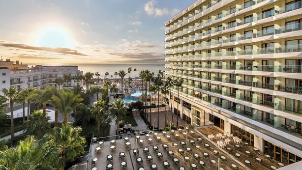 Un hotel con varios balcones, piscina y palmeras.
