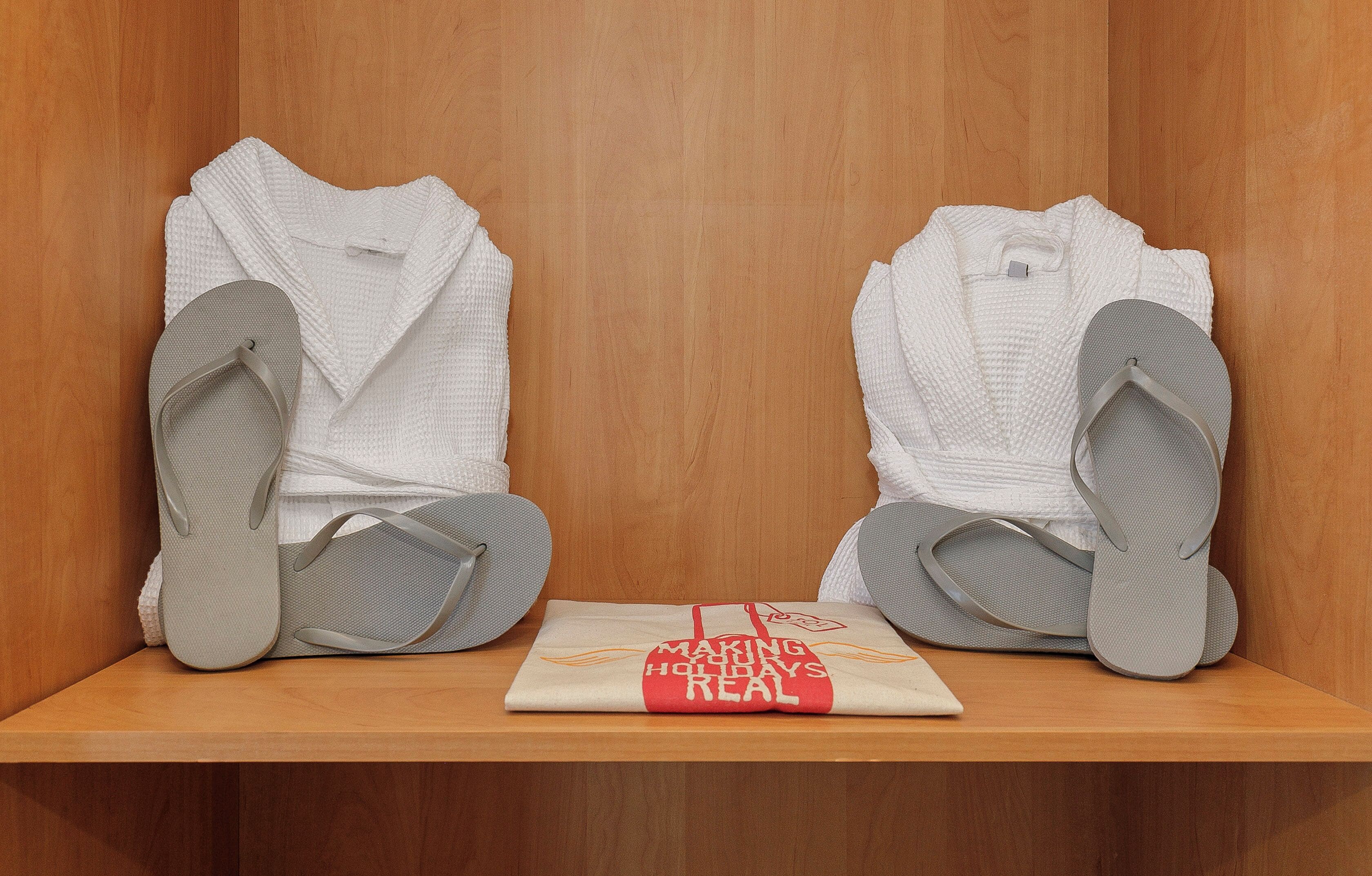 Een houten plank met twee witte badjassen en twee paar grijze slippers.