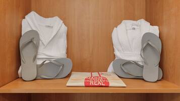 Een houten plank met twee witte badjassen en twee paar grijze slippers.