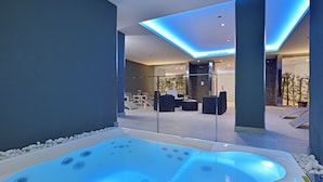 Un moderno espacio de spa con una bañera de hidromasaje, sillones reclinables y una zona de estar con paredes de cristal.
