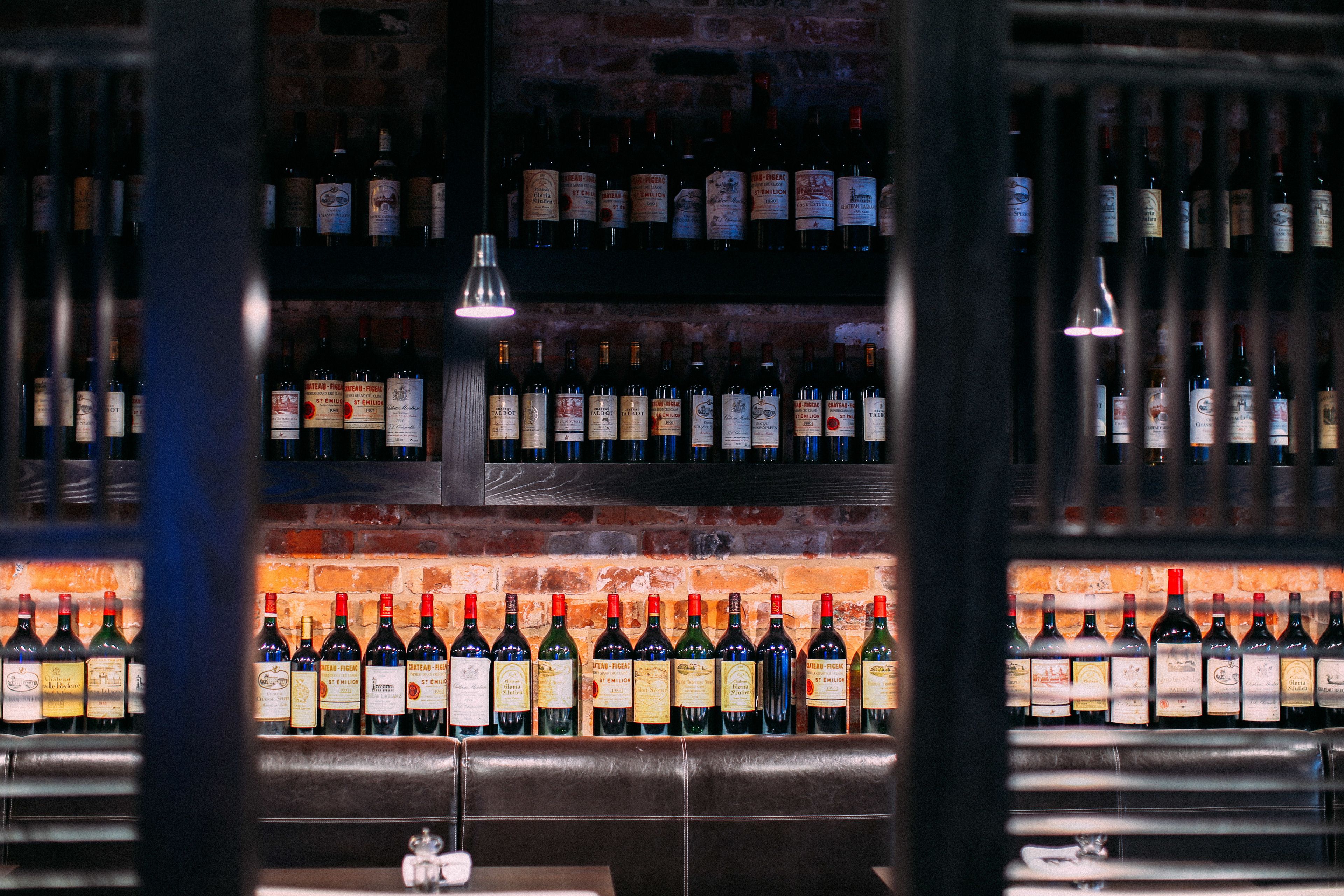 Een bar met verschillende wijnflessen op rekken, een bakstenen muur en een leren bank.