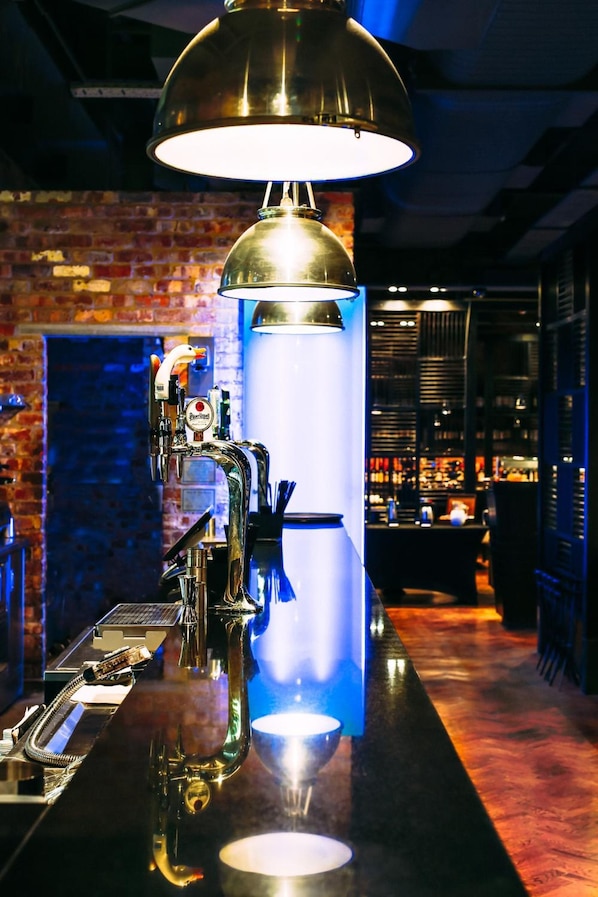 A bar area with a beer tap, a large illuminated light fixture, and a brick wall in the background. - mour Hotel (Nottingham)