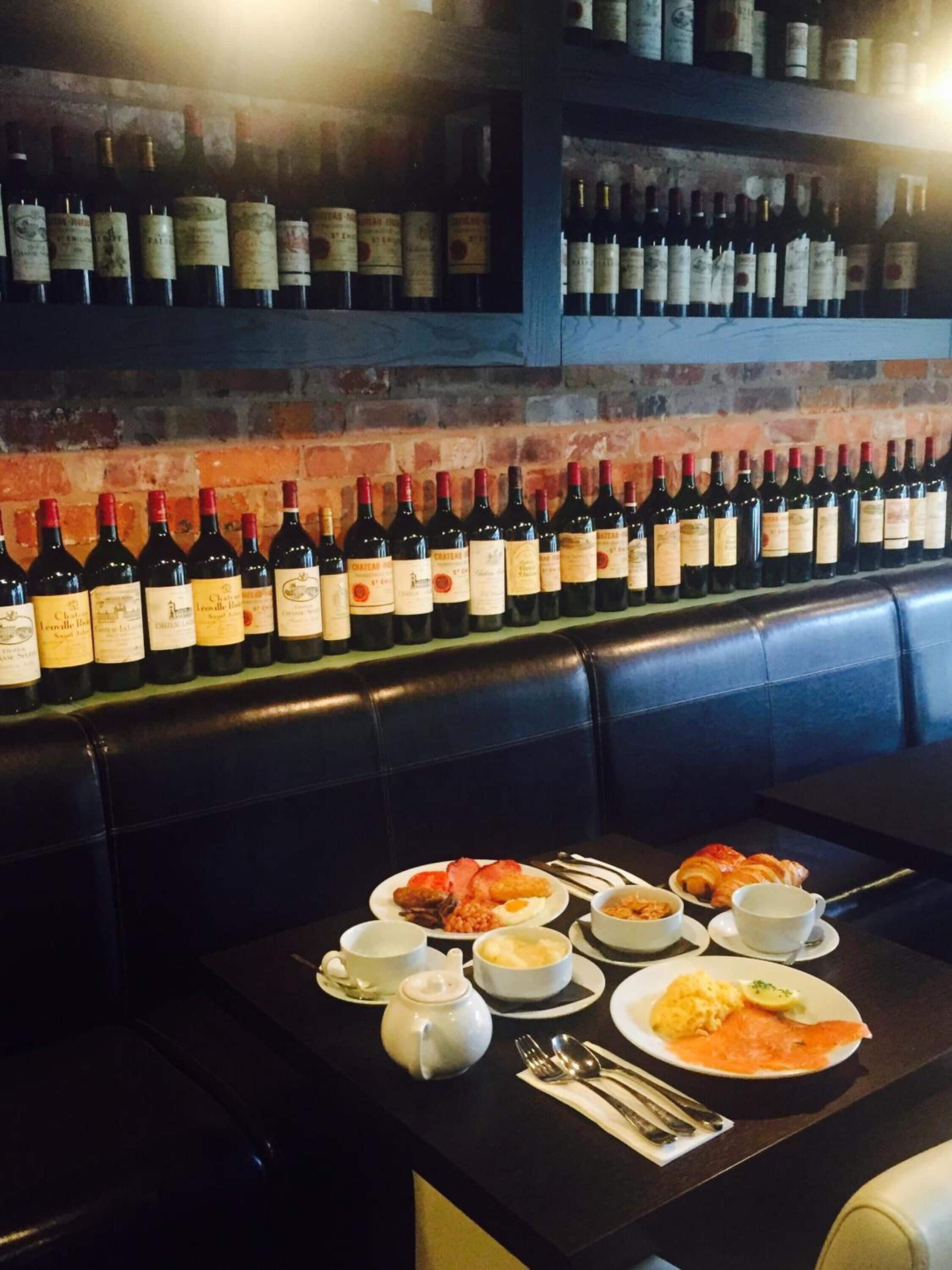 Un restaurante con una mesa larga preparada para una comida, mostrando platos de comida y una selección de botellas de vino en estantes al fondo.