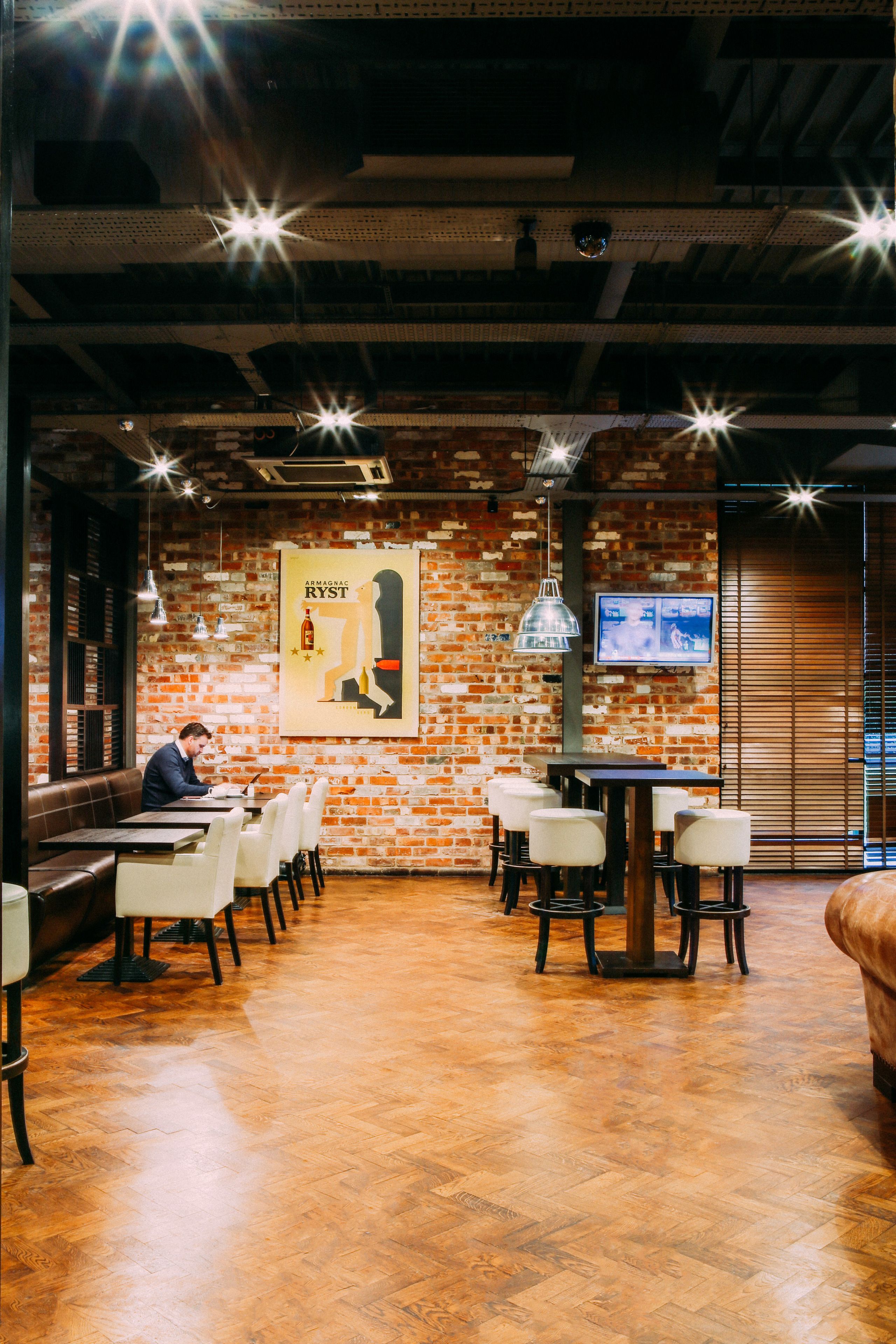 A restaurant with brick walls, wooden floors, and a TV mounted on the wall.