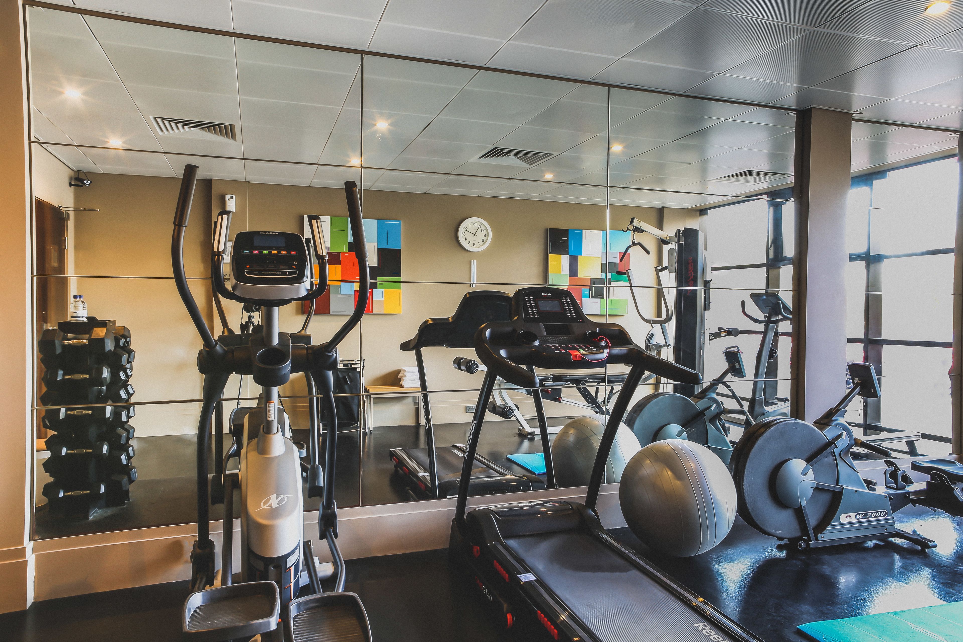 A gym with various exercise equipment, a clock on the wall, and a window with a view of the outside.
