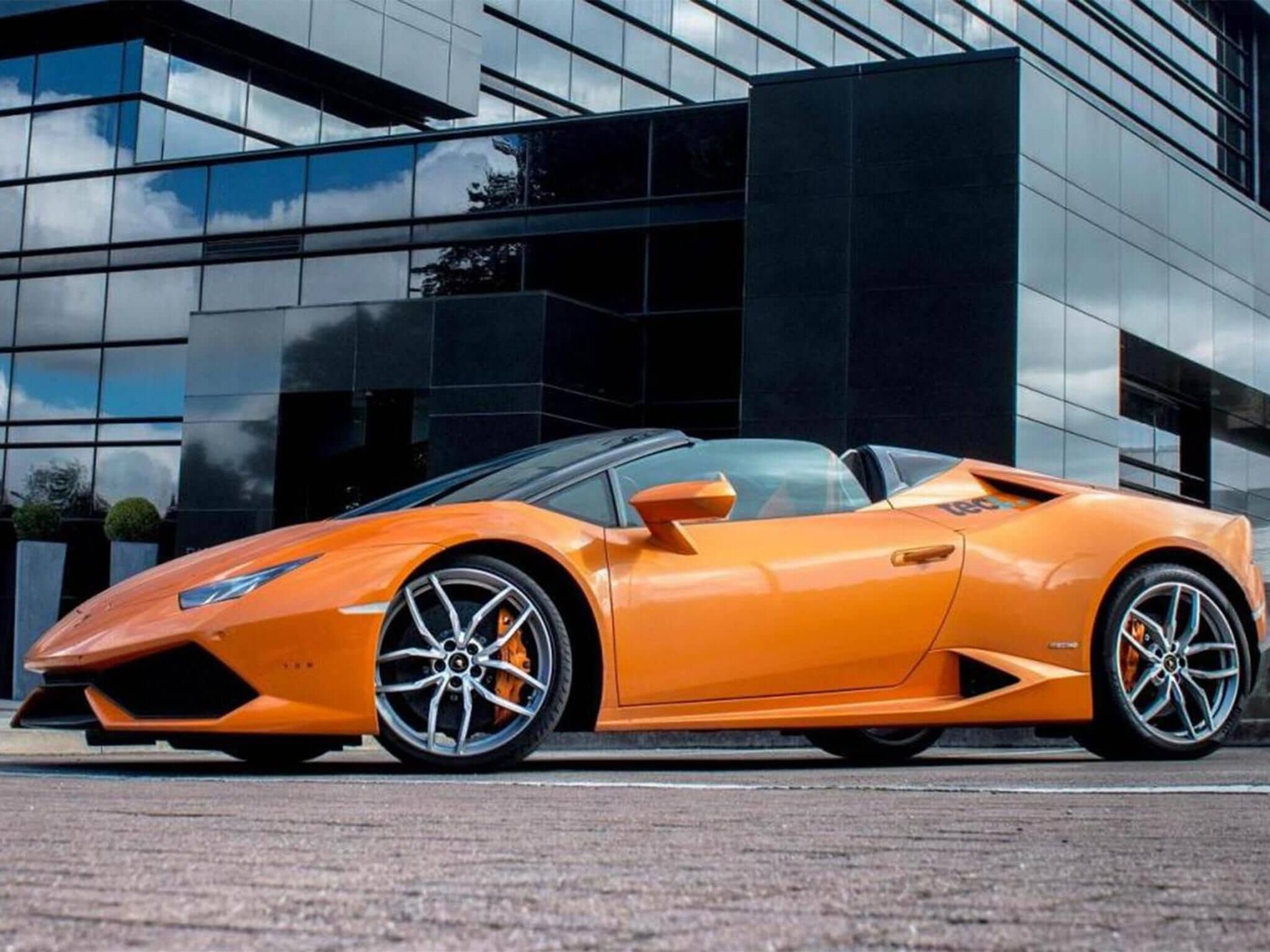 A modern building with reflective glass windows and a sleek orange sports car parked in front.