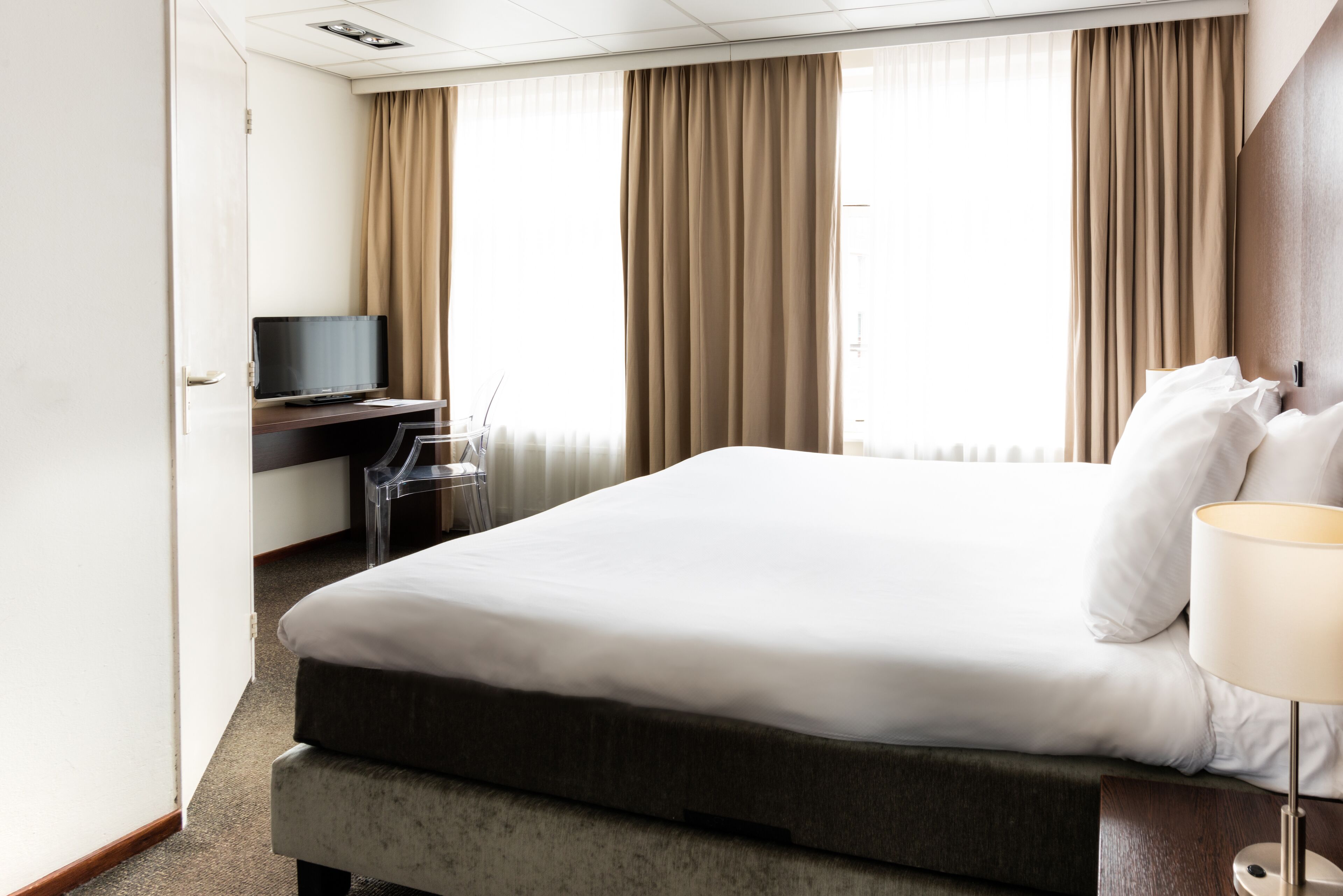 Una habitación de hotel con una cama grande, un escritorio y un televisor, y una lámpara.
