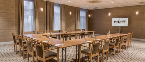 A conference room with long tables and chairs, a projector screen, and a patterned floor.