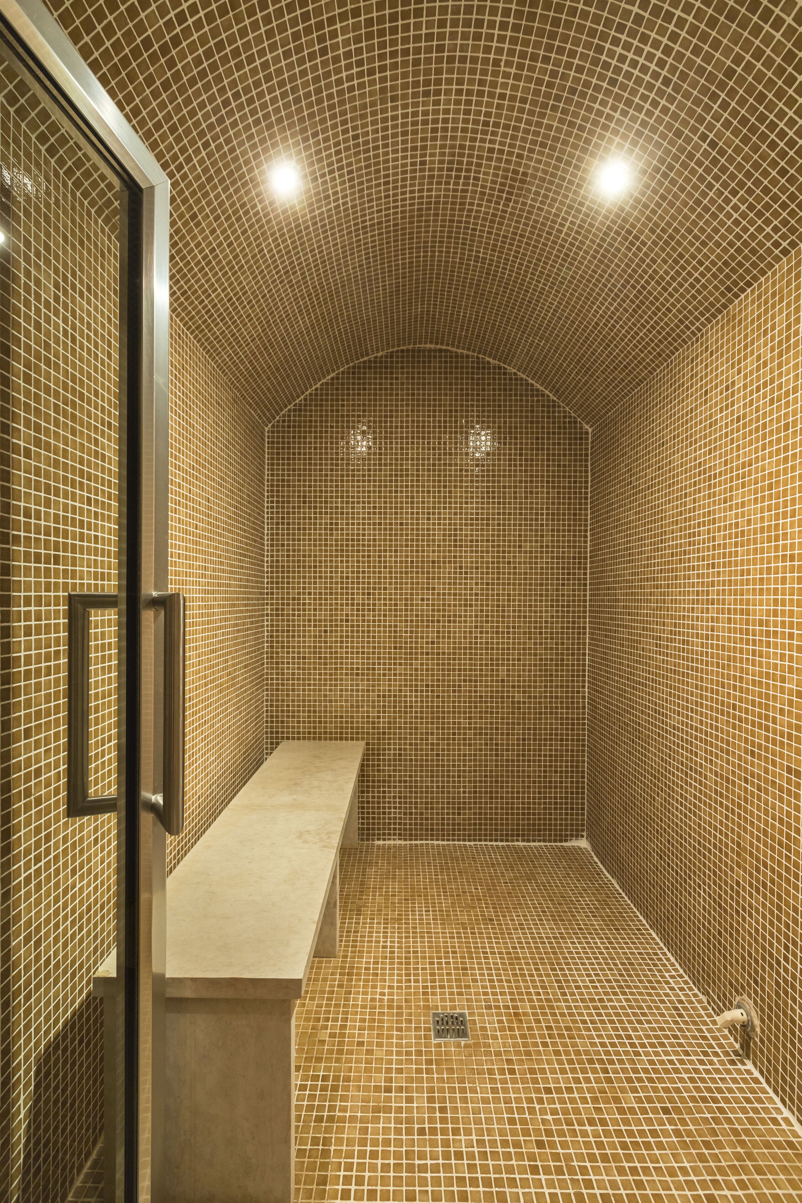 Un área de ducha con azulejos, un banco y una puerta de cristal.