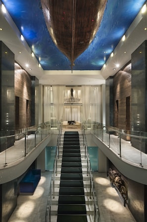 A modern interior with a central staircase, a ceiling mural, and a chandelier.
